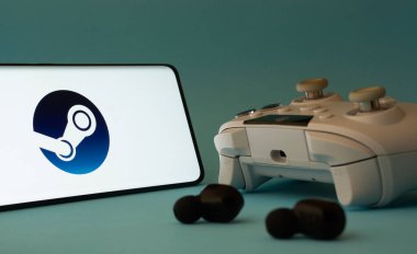 Dhaka, Bangladeş - 03 Haziran 2025: Buhar uygulaması simgesi ve mavi bir yüzey üzerinde kulaklıklar olan akıllı bir telefon.