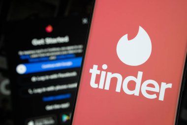 Dhaka, Bangladeş - 18 Mart 2025: Tinder logosu bir akıllı telefon ekranında gösterilir, arka planda bir bilgisayar ekranında Tinder giriş sayfası görünür.
