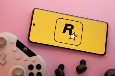 Dhaka, Bangladeş - 17 Haziran 2025: Rockstar oyun logosu, oyun kumandası ve pembe arka planda kulaklıkları olan akıllı telefon.