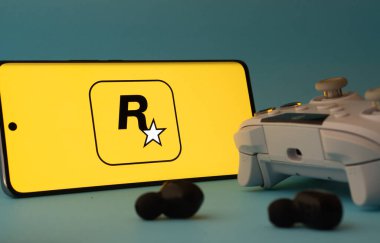 Dhaka, Bangladeş - 17 Haziran 2025: Mavi bir yüzey üzerinde bir denetleyici ve kulaklıklar yanında bir rockstar oyun uygulama simgesi ile akıllı telefon.