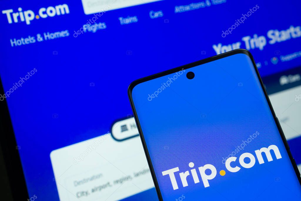 Dhaka, Bangladesh - 18 March 2025: The logo of the trip.com is displayed on a smartphone screen, and the website trip.com is visible on a computer screen in the background.