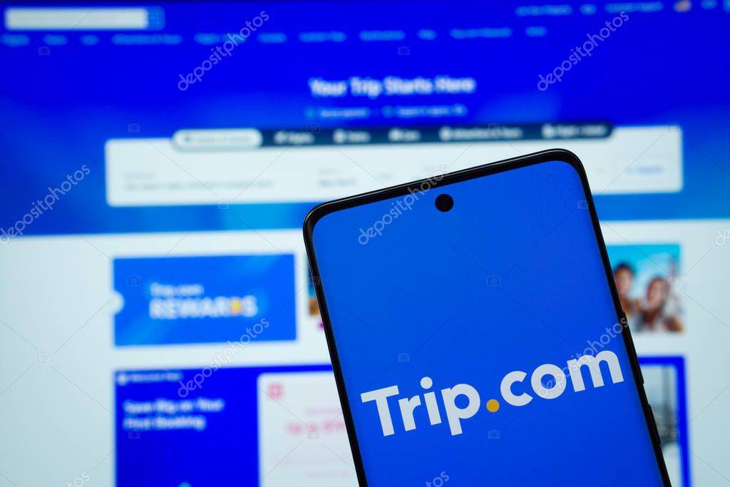 Dhaka, Bangladesh - 18 March 2025: The logo of the trip.com is displayed on a smartphone screen, and the website trip.com is visible on a computer screen in the background.