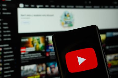 Dhaka, Bangladeş - 10 Temmuz 2025: Youtube logosu bir akıllı telefon ekranında gösterilir ve web sitesi arka planda bir bilgisayar ekranında görünür..