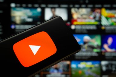 Dhaka, Bangladeş - 10 Temmuz 2025: Youtube logosu bir akıllı telefon ekranında gösterilir ve web sitesi arka planda bir bilgisayar ekranında görünür..