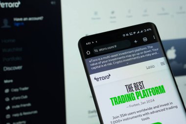 Dhaka, Bangladeş - 15 Temmuz 2025: eToro logosu akıllı telefon ekranında gösteriliyor ve eToro web sitesi arka planda bir bilgisayar ekranında görülebiliyor.