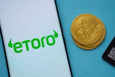 Dhaka, Bangladeş - 22 Haziran 2025: Bitcoin yakınlarındaki akıllı telefon ekranında eToro logosu ve mavi arkaplanda QR kodu.