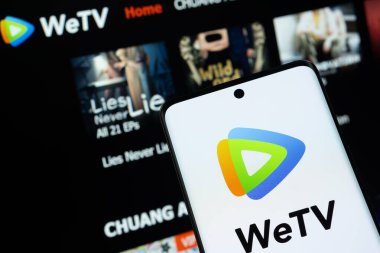 Dhaka, Bangladeş - 28 Temmuz 2025: WeTV logosu akıllı telefon ekranında gösteriliyor, web sitesi arka plandaki bilgisayar ekranında görülebiliyor.