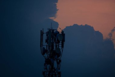 Siluetli baz istasyonu ve antenler karanlık bulutlu günbatımı gökyüzüne karşı.