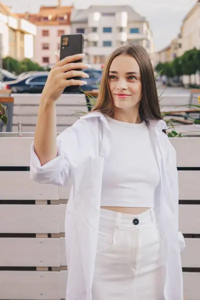 Uzun saçlı, beyaz saçlı güzel Avrupalı bir kız sokakta video çekiyor ya da video çekiyor. Dikey fotoğraf, sosyal ağlar konsepti.