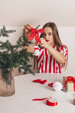 Güzel bir kız köknar dallarını kırmızı kumaş kurdeleyle süslüyor. Noel ve Yeni Yıl 'ı kutlamak, ekolojik tüketim, el yapımı