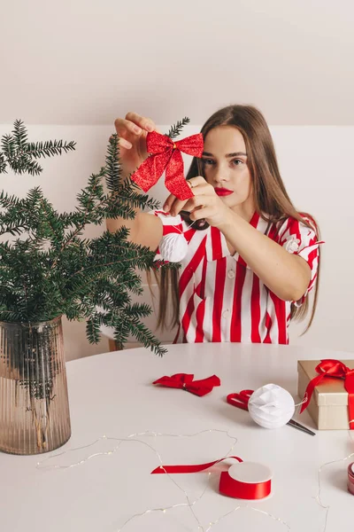 Güzel bir kız köknar dallarını kırmızı kumaş kurdeleyle süslüyor. Noel ve Yeni Yıl 'ı kutlamak, ekolojik tüketim, el yapımı