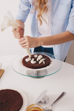 İnce elli genç bir kadın, özel bir stantta çikolatalı sünger keki doldurmak için pasta poşetinden tereyağı kremi sürüyor. Ev yapımı çikolatalı kek, geleneksel yemek pişirme, genç ev kadını.