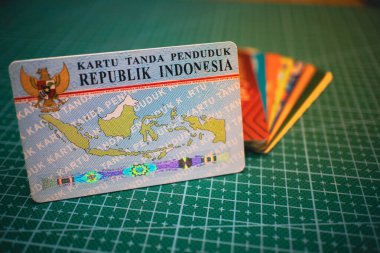 Blue Indonesian ID card (Kartu Tanda Penduduk) placed on a green grid background, representing official identity documentation, ideal for concepts related to personal identification and government services. clipart