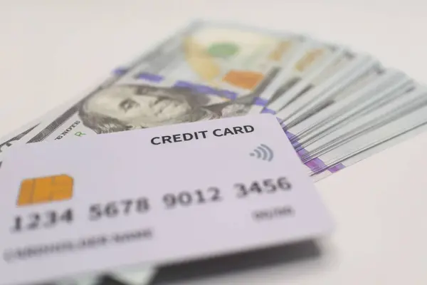 Beyaz kredi kartı, dijital ödemeler, finans ve Amerikan para birimi işlemlerini sembolize eden bir yığın mavi ve altın banknota yerleştiriliyor..