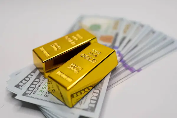 Zenginliği, finansal yatırımları ve küresel ekonomik işlemleri temsil eden bir yığın mavi ve altın banknota yerleştirilmiş parlak altın külçeler.