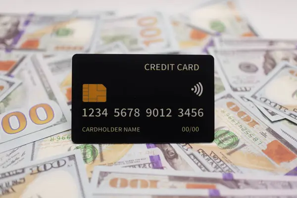 Dağınık Amerikan banknotlarının arka planına yerleştirilen siyah kredi kartı zenginliği, finansal güvenliği ve prim bankacılık hizmetlerini simgeliyor.