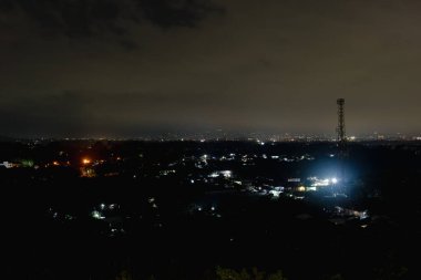 Nighttime lights of a village with cityscape in the distance, creating a serene, tranquil atmosphere. clipart