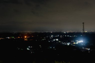 Şehir ışıkları karanlıkta parlıyor, sessiz bir gece manzarasının dingin güzelliğini yakalıyor..