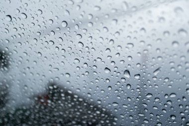 Bulutlu bir günde penceredeki yağmur damlalarının görüntüsünü kapatın, yağmur desenlerinin güzelliğini yakalayın.