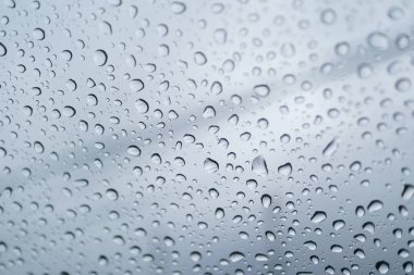 Penceredeki yağmur damlaları gri gökyüzü arkaplanına karşı, dokuyu ve yansımaları vurguluyor