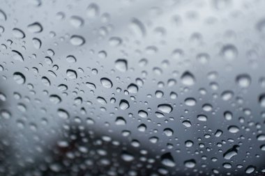 Penceredeki yağmur damlalarının desenli görüntüsü, su desenlerini ve atmosferik ambiyansı gösteriyor