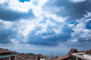 Dramatik bulutlu gökyüzünün altında sakin ve doğal bir atmosfer taşıyan kırsal bir köy manzarası