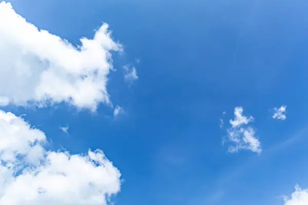 Pofuduk beyaz bulutlu parlak mavi gökyüzü, doğal güzelliği yansıtan huzurlu bir manzara.