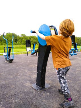 Şehir parkındaki ekipman üzerinde kızıl saç egzersizi yapan altı yaşında bir çocuk.