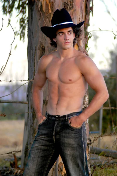一个有魅力的年轻牛仔脱下了他的衬衫 露出了肌肉 — 图库照片