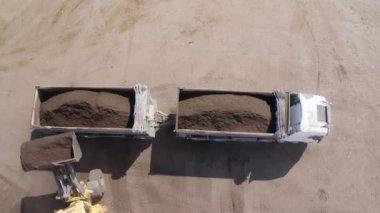 Endüstriyel gübre üretim alanı. Gübre yığınlarını ve traktörleri gösteren makineler gübre yüklüyor