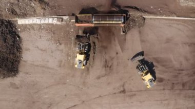 Endüstriyel gübre üretim alanı. Gübre yığınlarını ve traktörleri gösteren makineler gübre yüklüyor