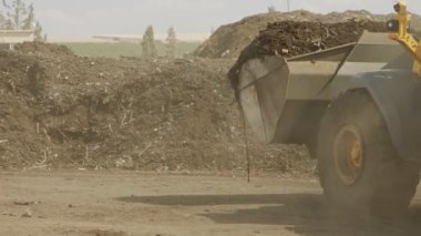 İndüksiyon gübre üretim alanı. Gübre yığınlarını ve traktörleri gösteren makineler gübre yüklüyor