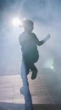 Dansçı yavaş çekimde hip hop dansı yapıyor, ışık ve duman arka planında.