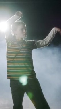Dansçı yavaş çekimde hip hop dansı yapıyor, ışık ve duman arka planında.