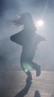 Dansçı yavaş çekimde hip hop dansı yapıyor, ışık ve duman arka planında.