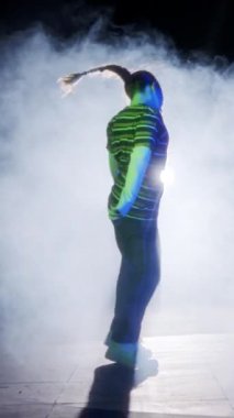 Dansçı yavaş çekimde hip hop dansı yapıyor, ışık ve duman arka planında.