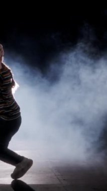 Dansçı yavaş çekimde hip hop dansı yapıyor, ışık ve duman arka planında.