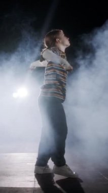 Dansçı yavaş çekimde hip hop dansı yapıyor, ışık ve duman arka planında.