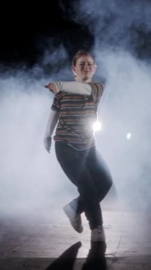 Dansçı yavaş çekimde hip hop dansı yapıyor, ışık ve duman arka planında.