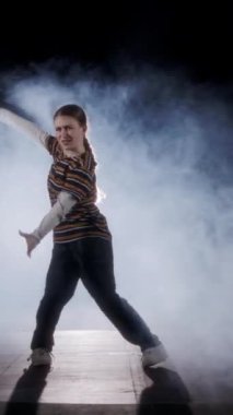 Dansçı yavaş çekimde hip hop dansı yapıyor, ışık ve duman arka planında.