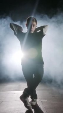 Dansçı yavaş çekimde hip hop dansı yapıyor, ışık ve duman arka planında.
