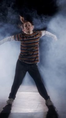 Dansçı yavaş çekimde hip hop dansı yapıyor, ışık ve duman arka planında.