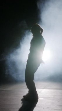 Dansçı yavaş çekimde hip hop dansı yapıyor, ışık ve duman arka planında.