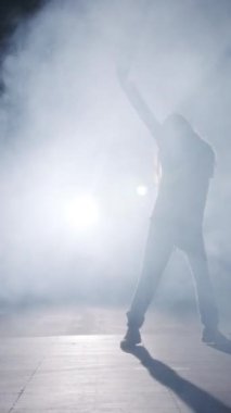 Dansçı yavaş çekimde hip hop dansı yapıyor, ışık ve duman arka planında.