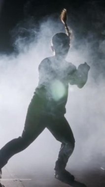 Dansçı yavaş çekimde hip hop dansı yapıyor, ışık ve duman arka planında.