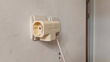 Duvarda beyaz bir fiş ve içinden beyaz bir kablo çıkıyor.