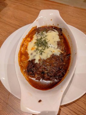 Beyaz kasede et tabağı olan beyaz bir tabak. Tabak peynirle kaplı ve üzerinde yeşil bir bitki var.