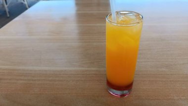 Bir bardak portakal suyu ahşap bir masada oturur. Bardağın yarısı dolu, pipet de içkinin içinde.