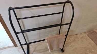 Üzerinde havlu olan siyah bir havlu askısı. Askı beton zeminde.