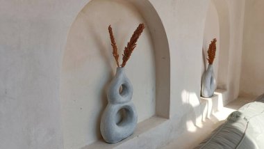 Kahverengi saplı iki vazo beyaz duvarlı bir odada sergileniyor.